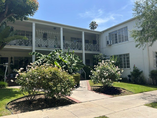A white building with a balcony and a tree in front.
